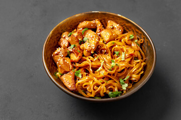 Udon noodles with chicken in teriyaki sauce in a brown bowl on a dark gray culinary background