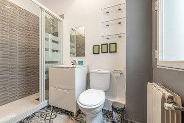 Bathroom with white resin sink, white wooden furniture, shower cabin with glass partition, rectangular frameless mirror, glass shelves and hydraulic tiles on the floor