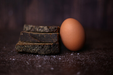 Pieces of black bread and a brown egg with sprinkled salt on a dark wooden background