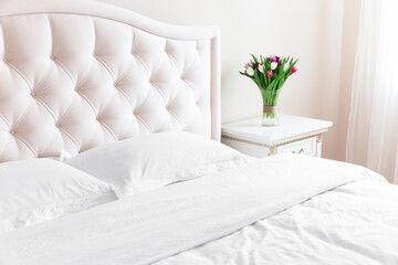 Bedroom with bed, white bedding, and bedside table with bouquet of tulips in a vase.