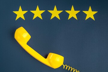 Five star rating and yellow retro phone on a blue background. Customer service quality control.