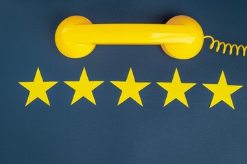 Five star rating and yellow retro phone on a blue background. Customer service quality control.