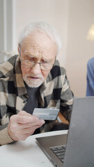 An elderly man learns to use a bank card for online shopping. He is taught by his young daughter
