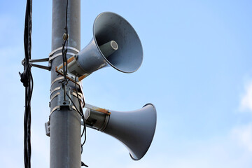 Loudspeakers on pole, alarm siren in city. Two public address system speakers on blue sky background - obrazy, fototapety, plakaty
