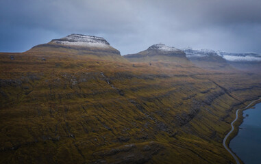 Aerial panoramic view of the fjord of Funningsfjordur with dramatic cloudy sky and snow-covered...