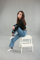 beautiful young woman on a gray background in black sunglasses. sit on a white chair. poses for a photo shoot