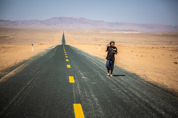 Person walking barefoot along a road while reading a book
