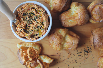 ricotta dip with sun-dried tomatoes and baked paprika in a ceramic white bowl and homemade popovers, which is a puffed, airy, and eggy hollow roll, is fresh from the oven