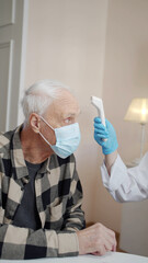 An orderly examines an elderly patient, measures the temperature and fills out a medical record