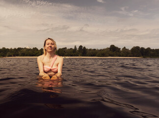 Young wet blonde woman in a swimsuit in dark water. Portrait of a woman in nature. brown tint