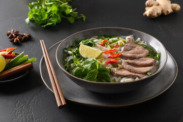 Pho Bo traditional Soup with beef, rice noodles, ginger, lime, chili pepper in bowl. Close up. Vietnamese and Asian cuisine.