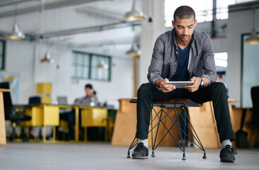 Hes a tech savvy young designer. Shot of a young man using a digital tablet while sitting in a modern office.