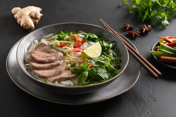 Pho Bo traditional Soup with beef, rice noodles, ginger, lime, chili pepper in bowl. Close up. Vietnamese and Asian cuisine.