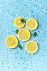 Round lemon slices in water with bubbles and green leaves. Cut citrus in carbonated blue soda. Concept of summer refreshing.
