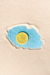 Fresh water and lemon slice surrounded by beach sand. Abstract concept of cool summer drink. Citrus fruit in beverage for thirsty, top view.
