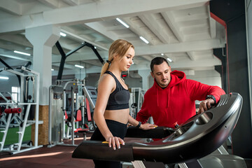Fototapeta na wymiar Male trainer talking to female client how work at treadmill in fitness club