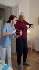 Fototapeta premium A woman puts a fitness band in the hands of an elderly man and tells how to use it during a workout