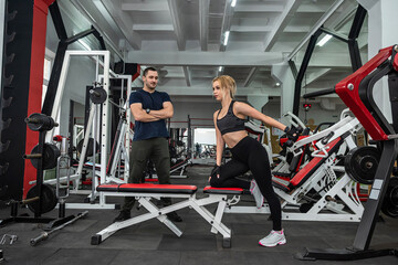 female client working out with a dumbbell under control of the personal male trainer at modern gym