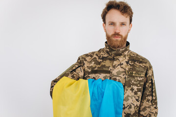 Portrait of an emotional young bearded Ukrainian patriot soldier in military uniform holding a flag...