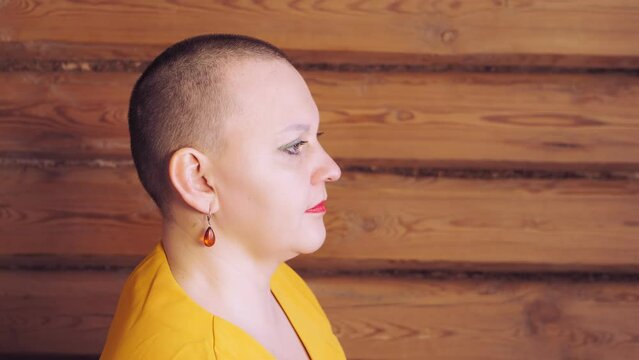 Stylish bald woman with bright make-up turns her head in profile to the camera. Medium plan