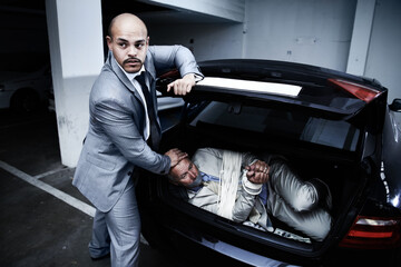 Captive to criminals. A gangster stuffing a bound and gagged businessman into the boot of his car.
