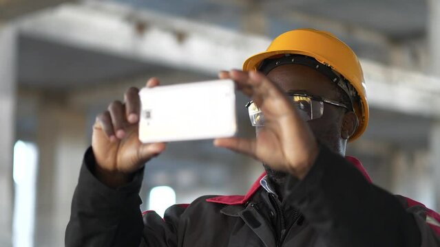 African american builder records videos on his smartphone. Worker at construction site filming a video
