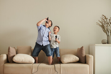 Two talented little brothers standing on sofa at home and singing into microphones