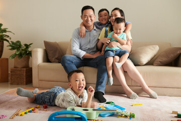 Little boy lying on floor and sticking out tongue when his parents and siblings sitting on sofa and...