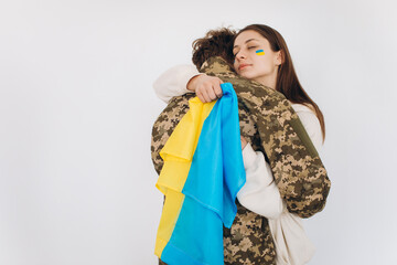 A Ukrainian girl hugs and holds a yellow and blue flag of a military man in uniform and says goodbye to him.
