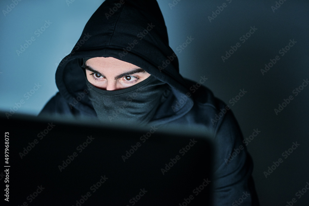 Poster hes on the hunt for your passwords. shot of a young hacker using a computer late at night.