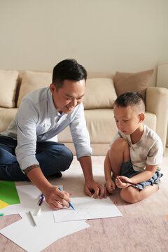 Happy father enjoying helping little son with drawing picture for kindergarten