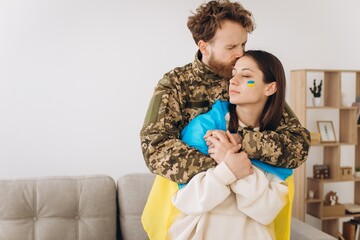 Ukrainian couple, military man in uniform hugs and wraps his wife in the Ukrainian flag. The concept of patriotism.
