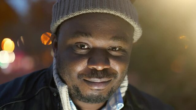 Slow Motion Cheerful african american man in winter hat looks at the camera and smiles shyly