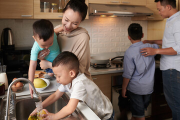 Sons helping mother and father with cooking breakfast, they are rinsing fruits and frying eggs