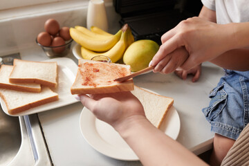 Hands of mother teaching little son speading jam on sandwich bread