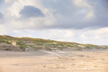 Coastal landscape Dutch North Sea coast during sunrise with old and new dunes smoothed by storm winds and overgrown with marram grass and shadows and sunlit dune tops