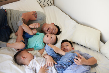 Joyful father and his three sons relaxing on bed when spending weekend together at home