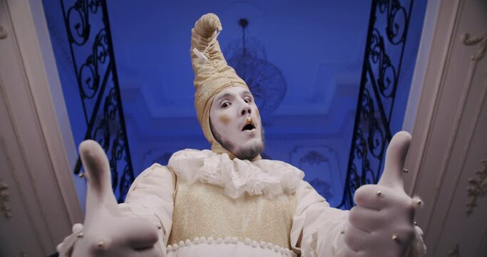 A make-up cool dramatic funny mime guy on a blue theatrical stage shows thumbs up gesture. A theater actor dressed as an old Baroque harlequin. Copy space theme for promo video. Wow reaction