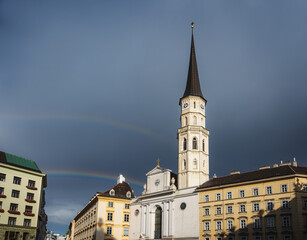Fototapeta na wymiar Saint Michael Church at Saint Michael Square (Michaelerplatz) with a rainbow in the sky - Vienna, Austria