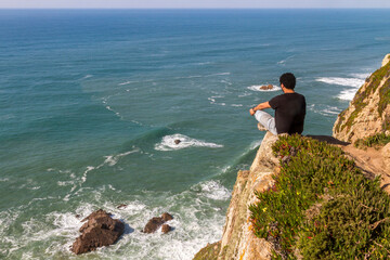 Junger Mann sitzt auf einem Felsen über dem Atlantik
