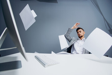 handsome man working at the computer in the office scatters documents Gray background