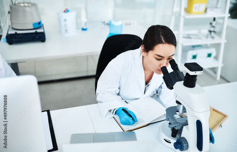 Poster Writing drug trial methodologies. Shot of a young scientist writing notes while using a microscope in a lab.