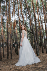 Obraz na płótnie Canvas A beautiful, satisfied bride in a pine forest poses.