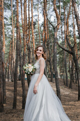 Obraz na płótnie Canvas A beautiful, satisfied bride in a pine forest poses.