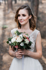 A beautiful, satisfied bride in a pine forest poses.