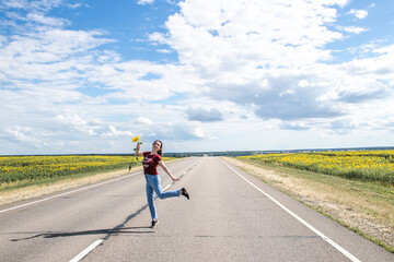 Fototapeta premium a girl stands on the road and holds a sunflower