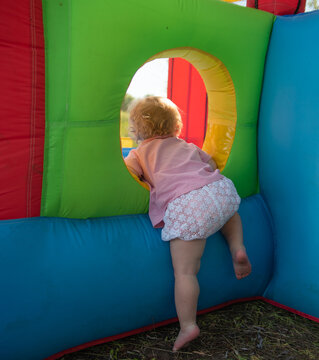 The Kid Climbs Into The Bouncy Castle Through A Round Window In The Summer Barefoot