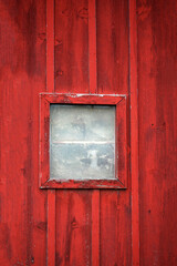Square dirty weathered window on aging red wooden wall with paint beginning to peel