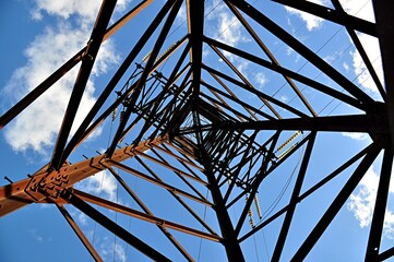 Metal support of high-voltage lines. A low angle view of the metal lattice poles of power lines against a blue sky. - Powered by Adobe