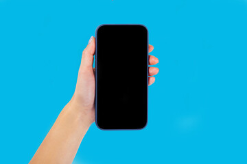 A modern smartphone with a blank screen for a layout in the hands on a blue background, top view with free space